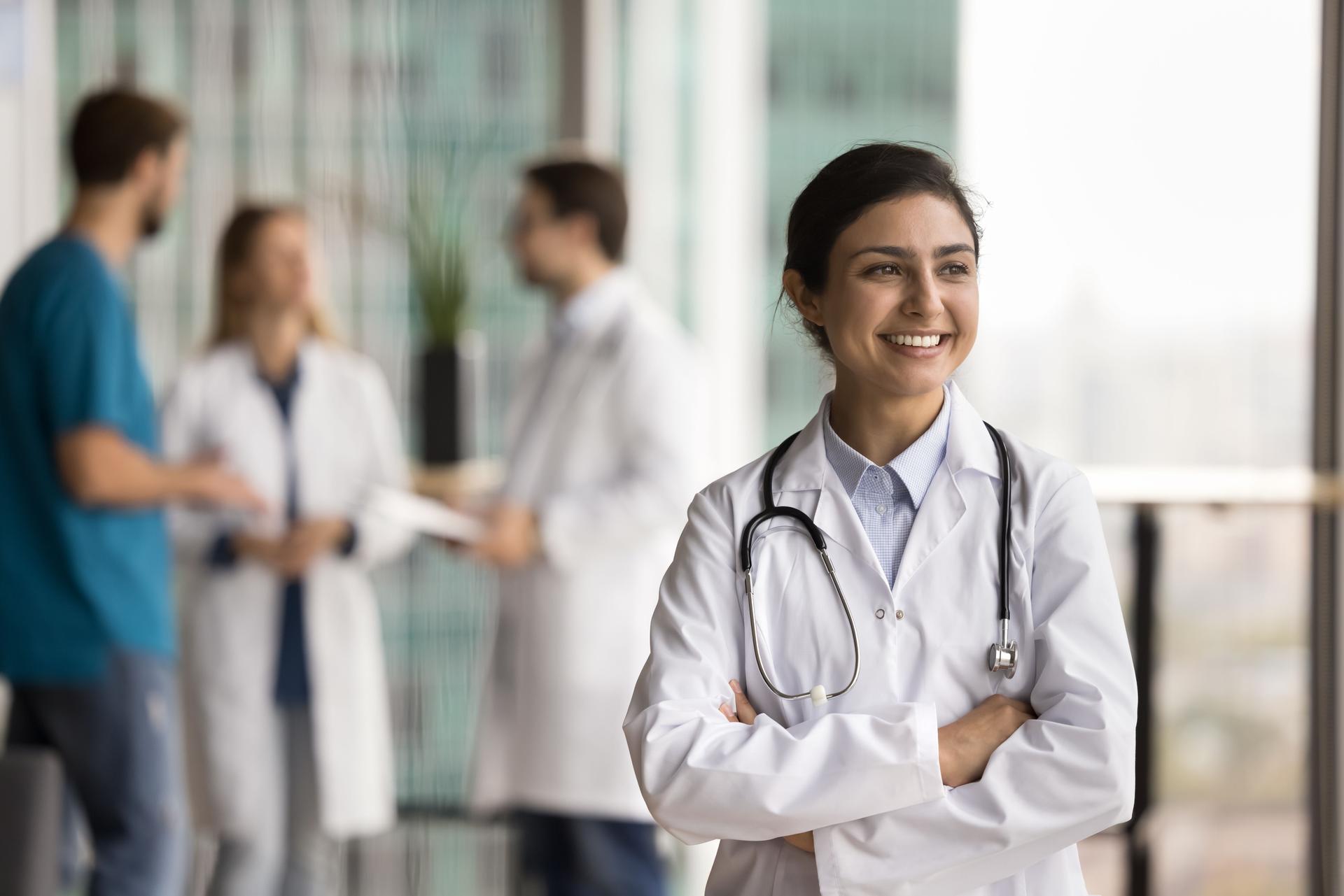 Happy dreamy young Indian doctor woman posing in clinic hall